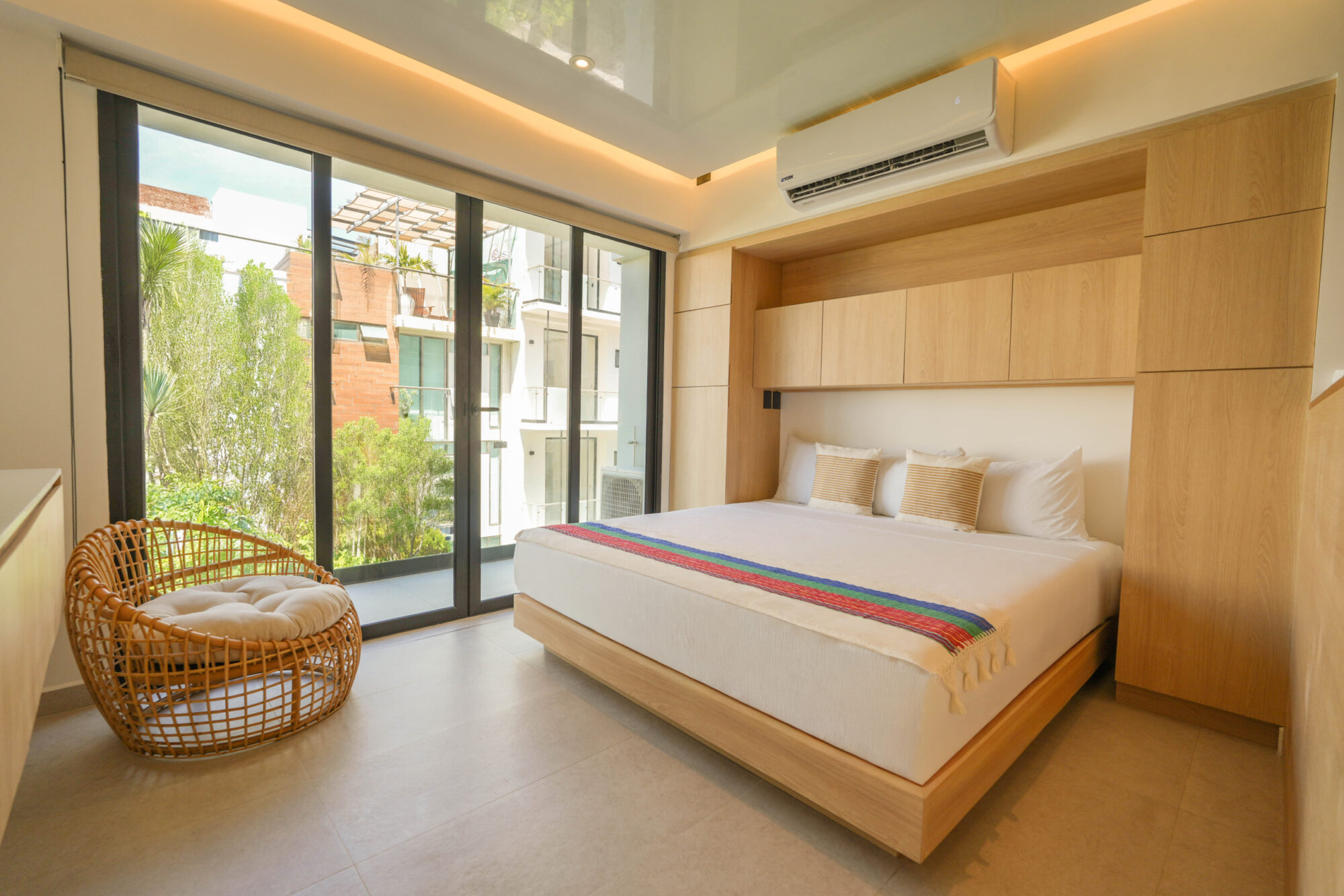 Habitación de diseño contemporáneo con acabados en madera, ventanales amplios y vista a un entorno natural, dentro de un desarrollo residencial de lujo con departamentos en venta en Playa del Carmen, creados para disfrutar confort, estilo y conexión con el entorno caribeño.