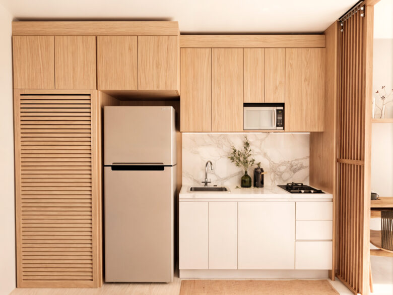 Cocina moderna del desarrollo Macondo Punta Esmeralda con acabados en madera natural, barra de mármol blanco, microondas, refrigerador y decoración minimalista, dentro de los departamentos en venta en Playa del Carmen.