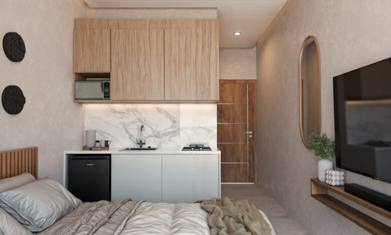 Estudio del desarrollo Macondo Punta Esmeralda con cama, cocineta moderna de mármol y madera, televisión de pantalla plana y decoración minimalista en tonos neutros, parte de los departamentos en venta en Playa del Carmen.