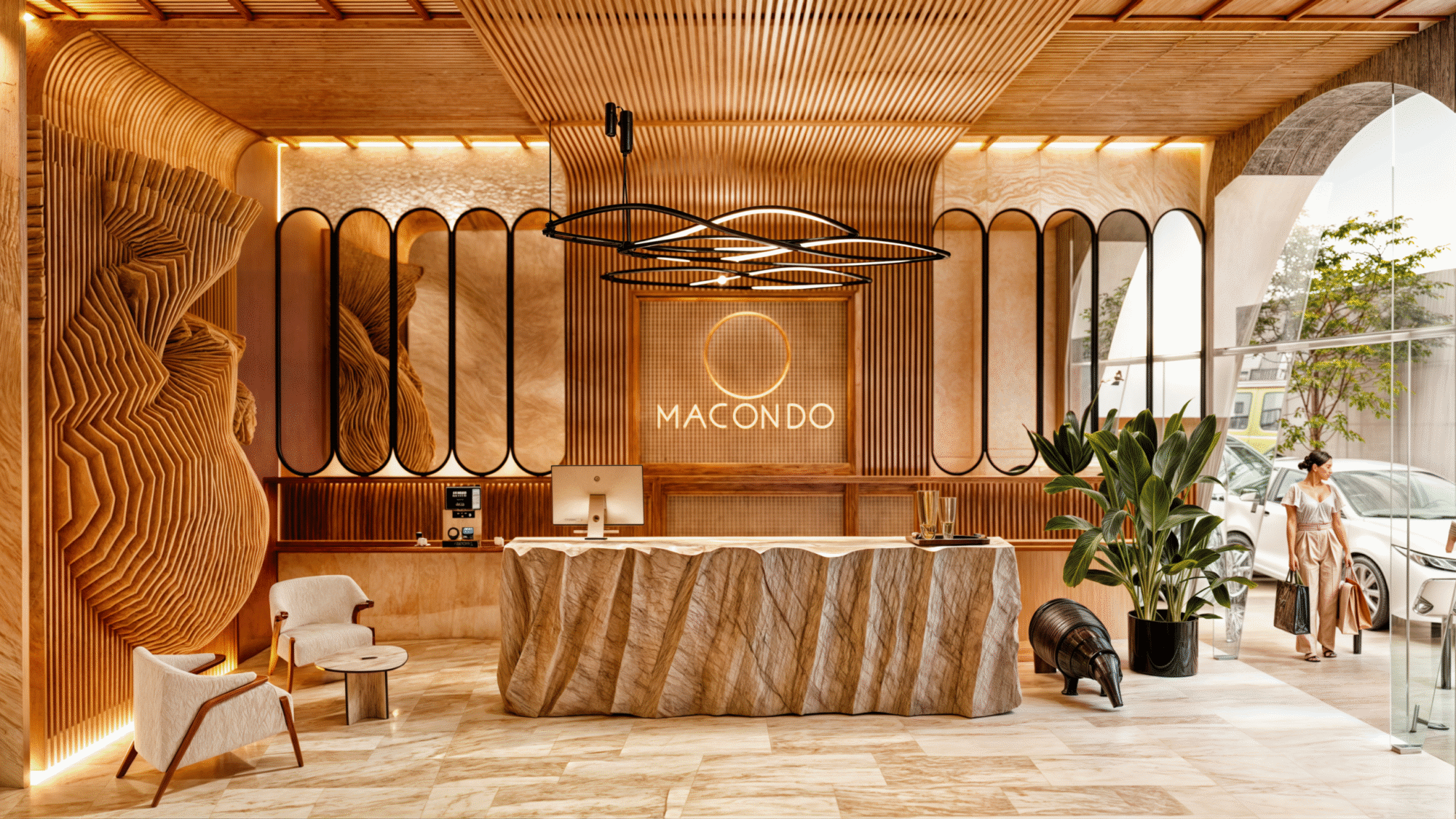 Lobby de Macondo Corazón en Playa del Carmen, con diseño interior en tonos cálidos, paredes y mobiliario de madera tallada, iluminación ambiental dorada, plantas decorativas, recepción con acabado orgánico en piedra y ventanales amplios hacia la calle. Un espacio que refleja la sofisticación de los departamentos en venta en Playa del Carmen.