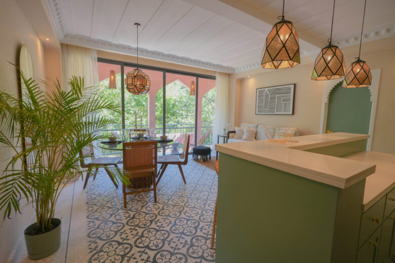 Área de comedor y sala de estar en una unidad de Pink Riad Tulum, con mosaicos artesanales en el piso, lámparas geométricas de estilo marroquí y ventanales que se abren a la naturaleza. Un ambiente luminoso dentro de los departamentos en venta en Tulum.