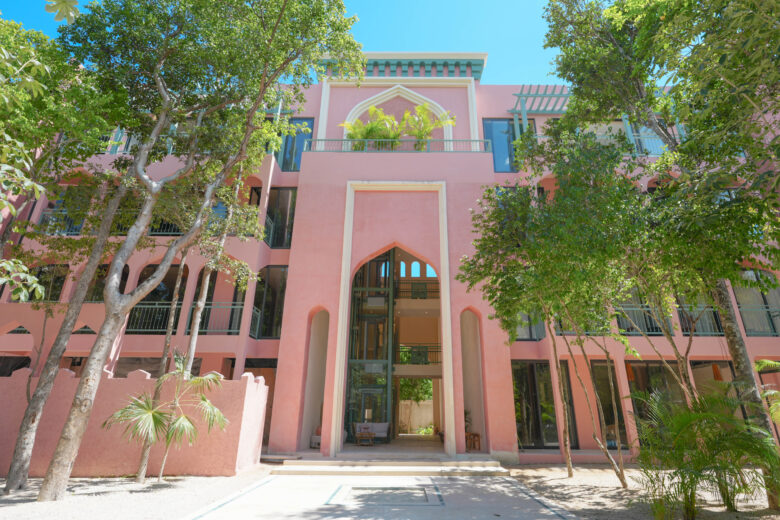 Fachada de Pink Riad Tulum con arcos característicos del diseño marroquí, acabados en tonos rosados y rodeada de vegetación tropical. Un desarrollo boutique con departamentos de lujo en venta en Tulum, donde el arte y la arquitectura se fusionan con la naturaleza.