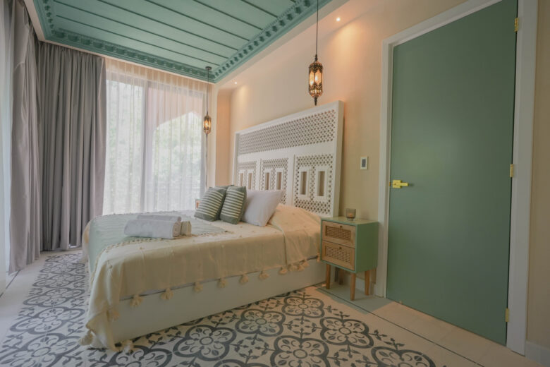 Habitación principal en una unidad de Pink Riad Tulum, con techo verde menta, lámparas de metal calado, textiles naturales y luz suave filtrándose entre cortinas vaporosas. Espacio íntimo dentro de los departamentos en venta en Tulum.